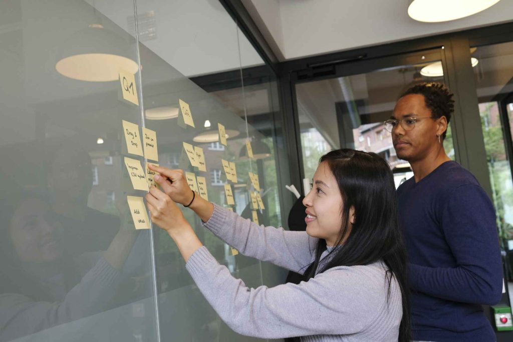 2 professionals sticking notes on board at work